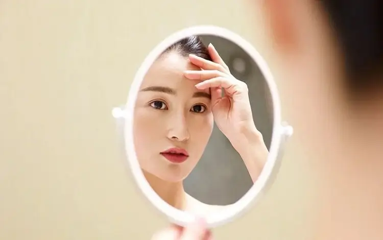 Phụ Nữ Kiểm Tra Tình Trạng Da Khô Nẻ Khi Chăm Sóc Da Đúng Cách Trước Gương